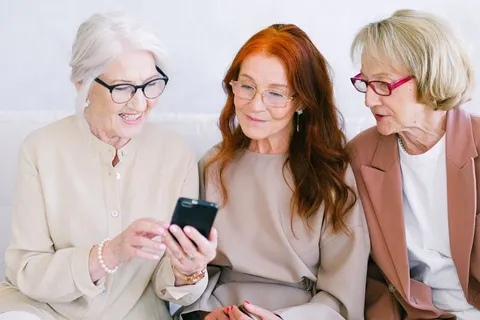 Three older women look at a smartphone together and smile.