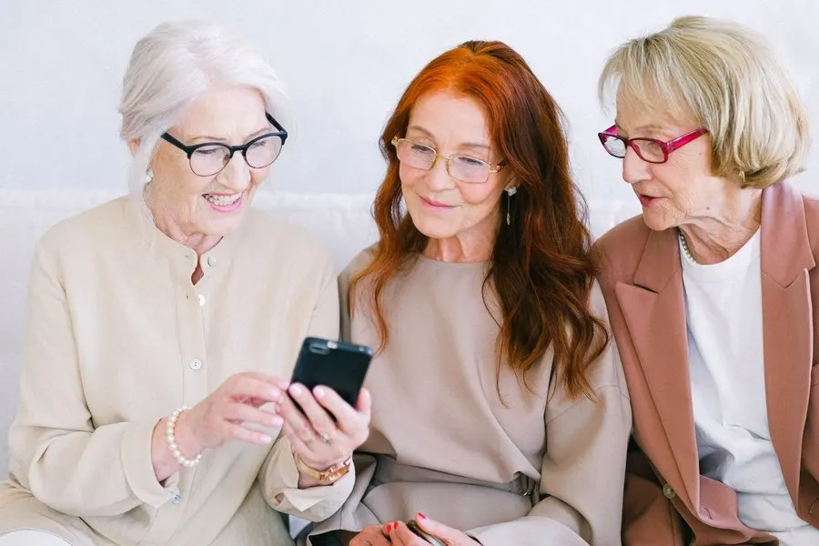 Three older women look at a smartphone together and smile.