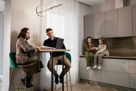 Two adults at a tall table review papers and a laptop while two children sit nearby.